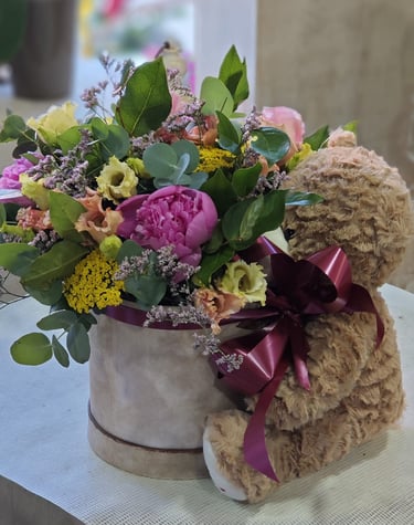 A floral arrangement Valentine's day in a gift box with a teddy bear and pink peonies.