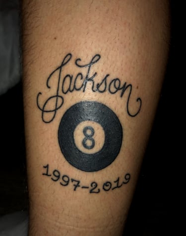 Tattoo of black script of Jackson above an 8 ball with the dates 1997-2019 beneath