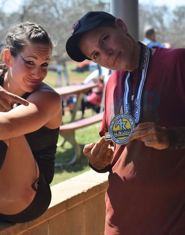 Two athletes celebrating with an Atlas Race finisher medal at an outdoor obstacle course event.