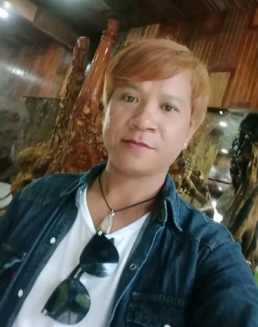 Man smiling indoors in Pattaya, Thailand, wearing a denim shirt and sunglasses on a white T-shirt.