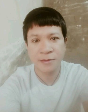 Male massage therapist wearing a light shirt, looking at the camera indoors with a calm expression and soft lighting.