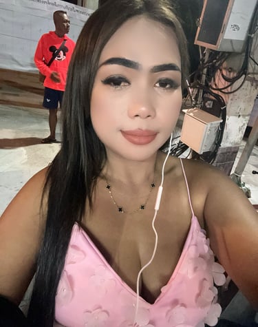 Lady wearing a pink top with headphones in left ear and a man standing in the background