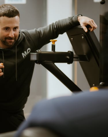 Personal trainer in hoodie coaching client on gym equipment in Leamington Spa fitness centre, focused on technique and su