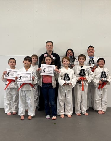 Martial arts instructor with students holding karate achievement certificates and trophies in a dojo.
