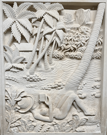 Hand-carved stone relief showing a woman reading under palm trees on a tropical beach.