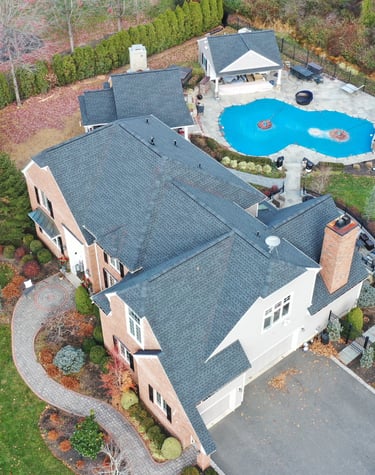 Aerial view of a luxury brick home with a new charcoal asphalt shingle roof and backyard swimming pool.
