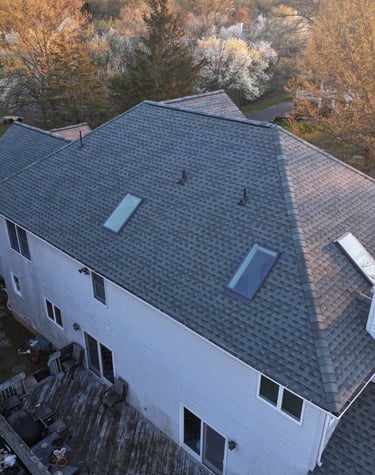 Aerial view of a suburban house featuring a new grey asphalt shingle roof with skylights.