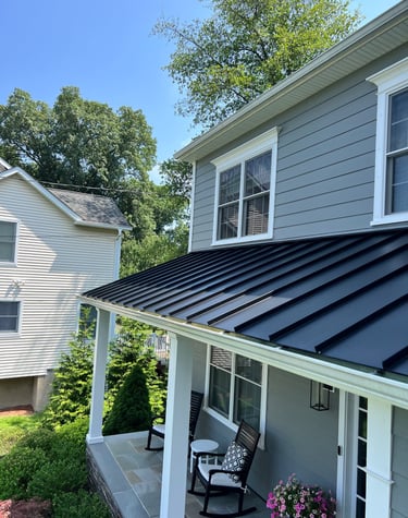 Modern black standing seam metal roof installed on a grey house porch with white columns.