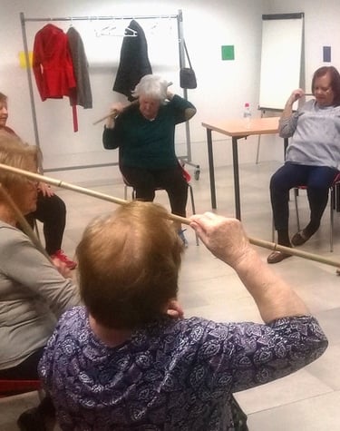 Un grupo de personas mayores está sentado en círculo realizando ejercicios de movimiento para mejora