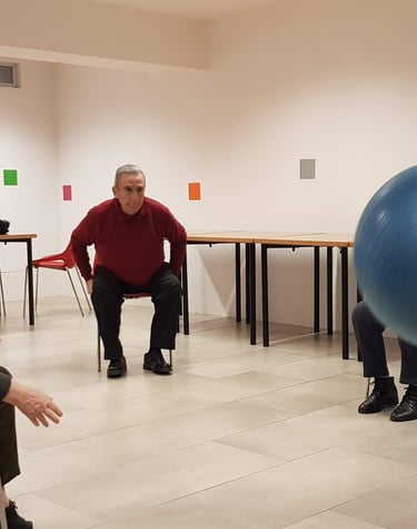 Un grupo de personas mayores está sentado en círculo realizando ejercicios con una pelota como parte