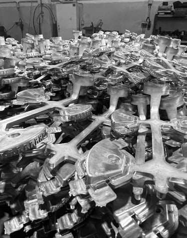 A large collection of industrial aluminum die cast parts stacked in a manufacturing factory workshop.