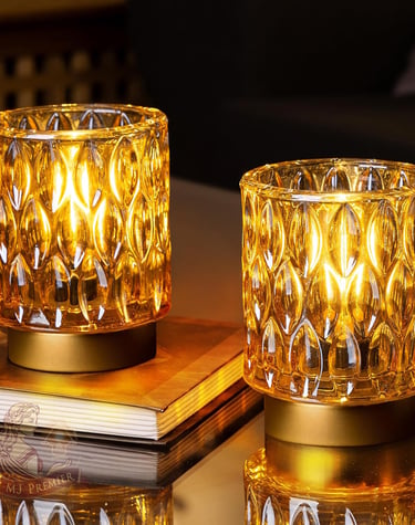 Two amber glass hurricane candle holders with decorative textured patterns glowing on a table.