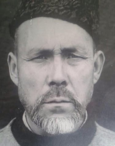 Vintage black and white portrait of an elderly man with a beard wearing a traditional hat.