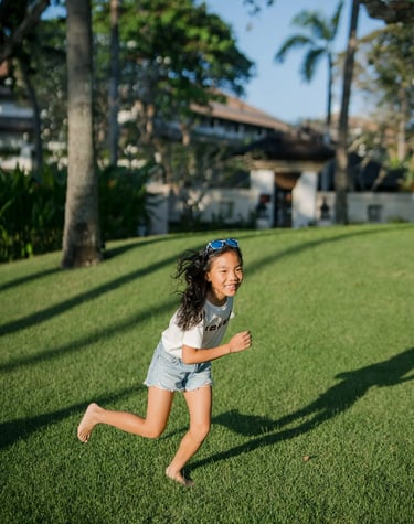 Young girl running across the lawn during a family photography session at InterContinental Bali Resort