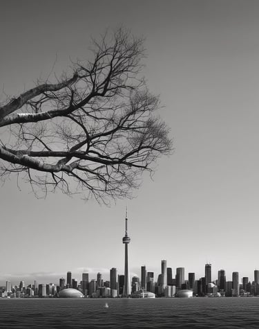 A modern building with a teal-green glass facade, positioned at an angle against a partially cloudy sky. The building has numerous windows and a Canadian flag is mounted at the top.
