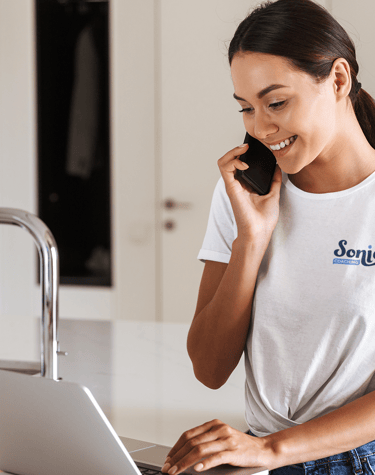Femme souriante en t-shirt blanc avec un logo de coaching imprimé, parlant au téléphone.