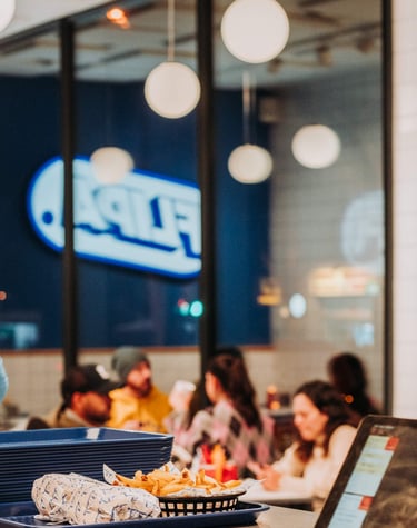 Clientes comiendo en Flipa con el logo iluminado reflejado en el cristal