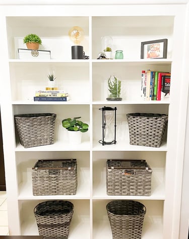 An organized bookshelf, decorated with plants and wicker baskets organized by Flawl