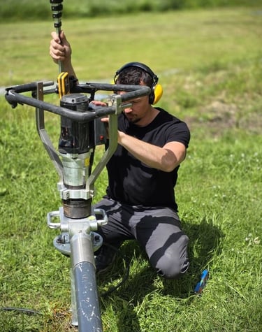 Professional technician installing a helical screw pile foundation using a portable power drive tool.