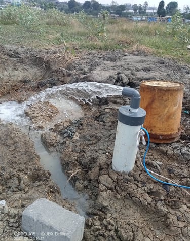 Agricultural water well pump discharging fresh water into a dirt irrigation trench in a field.