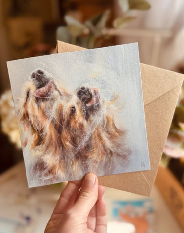 A square shape greeting card featuring a design of two golden retrievers playfully licking a window