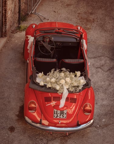 Auto d’epoca rossa decorata con fiori bianchi e nastri, pronta per il matrimonio