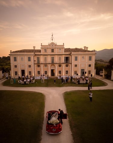 Arrivo degli sposi in auto d’epoca davanti a una villa storica illuminata al tramonto.