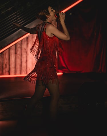 Jessie BaréKa chante sur scène en robe rouge à franges, ambiance cabaret.