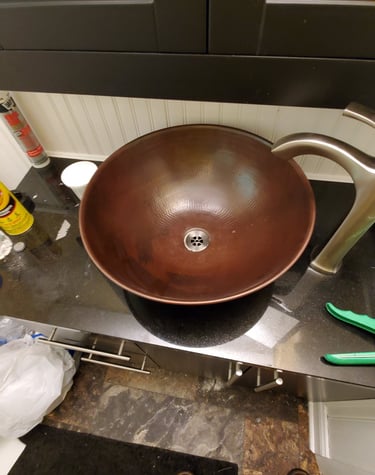 Hammered copper vessel sink installed on a black granite countertop with a brushed nickel faucet.