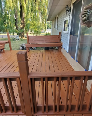 Freshly stained brown wooden deck with built-in benches and railings outside a residential home.