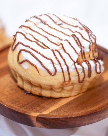 Rol de canela recién horneado con glaseado blanco y un chorrito de chocolate sobre un pedestal