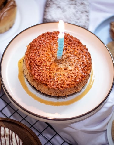 Pastel de flan con caramelo y una vela de cumpleaños encendida, rodeado de una variedad de galletas 