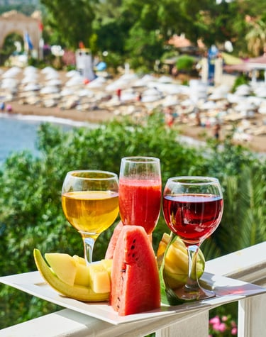 Refreshing summer drinks and sliced fruit platter on a balcony overlooking a tropical beach resort.