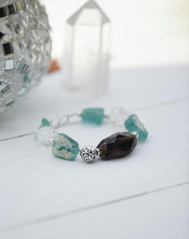 Pulsera de cuentas hecha a mano con cristal marino turquesa y cuarzo ahumado sobre una superficie blanca.