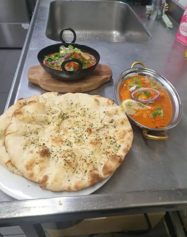 Authentic Indian butter chicken and lamb curry served with fresh garlic naan bread on a metal kitchen counter.