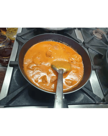 Authentic butter chicken curry simmering in a black frying pan on a gas stovetop.
