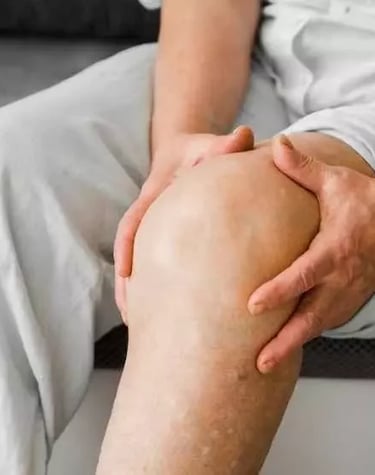 Homem mais velho sentado na cama com ambas as mãos na região do joelho