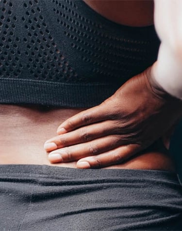 Mulher vestindo roupa de treino com dor na região lombar