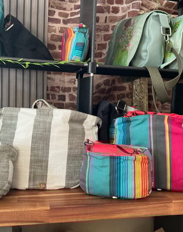 Handmade colorful striped canvas shoulder bags and crossbody purses displayed on a boutique wooden shelf.