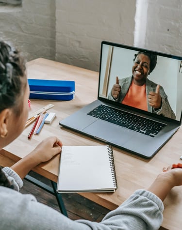 A young student participating in a virtual Tutoring session on a laptop with an encouraging Teacher.
