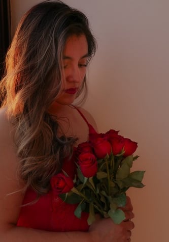 Una mujer con cabello largo y ondulado sosteniendo un ramo de rosas rojas con una iluminación calida