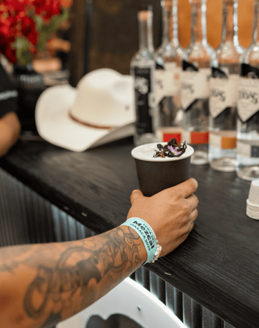 A person with a tattooed arm holds a mezcal cocktail at the Feria del Mezcal Oaxaca 2023 festival.