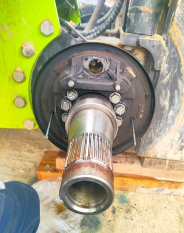 Close-up of a heavy machinery axle shaft and brake assembly undergoing mechanical repair.