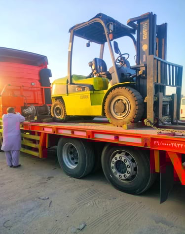 A yellow Clark forklift secured on a red flatbed trailer for heavy machinery transport.