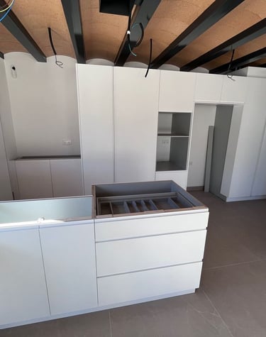 Cuisine moderne blanche avec placards sans poignées, îlot central et plafonds industriels voûtés