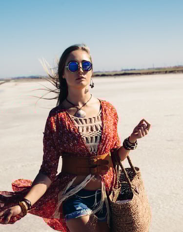 a woman in a red dress and sunglasses walking on a beach