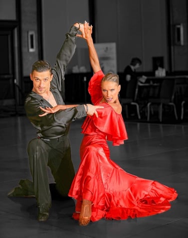 A man in a black satin shirt is kneeling with a woman in a red satin dress on the dance floor