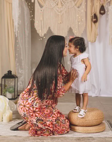 una mamá hincada y su niña pequeña parada, tocándose nariz con nariz