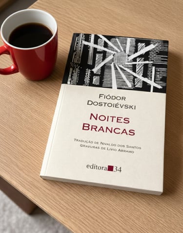 A copy of White Nights by Fyodor Dostoevsky on a wooden table next to a red mug of black coffee.