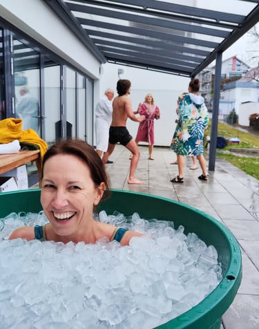 Eine Frau sitzt lachend und fröhlich in einem Eisbad gefüllt mit Eiswürfeln